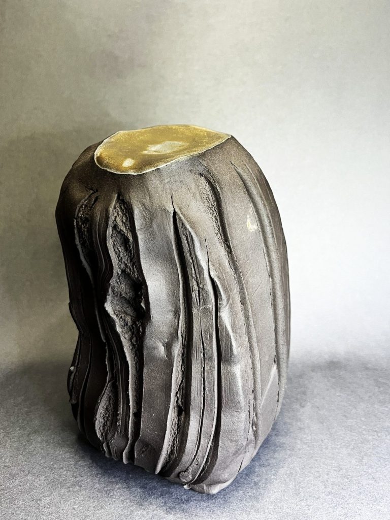 Keramikskulptur aus schwarzem Ton, seitlich geritzt mit Rosendornen, raue Textur, oben goldene, glatte Oberfläche